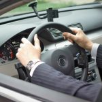 Businessman driving a car at the street. Two hands on a steering wheel.